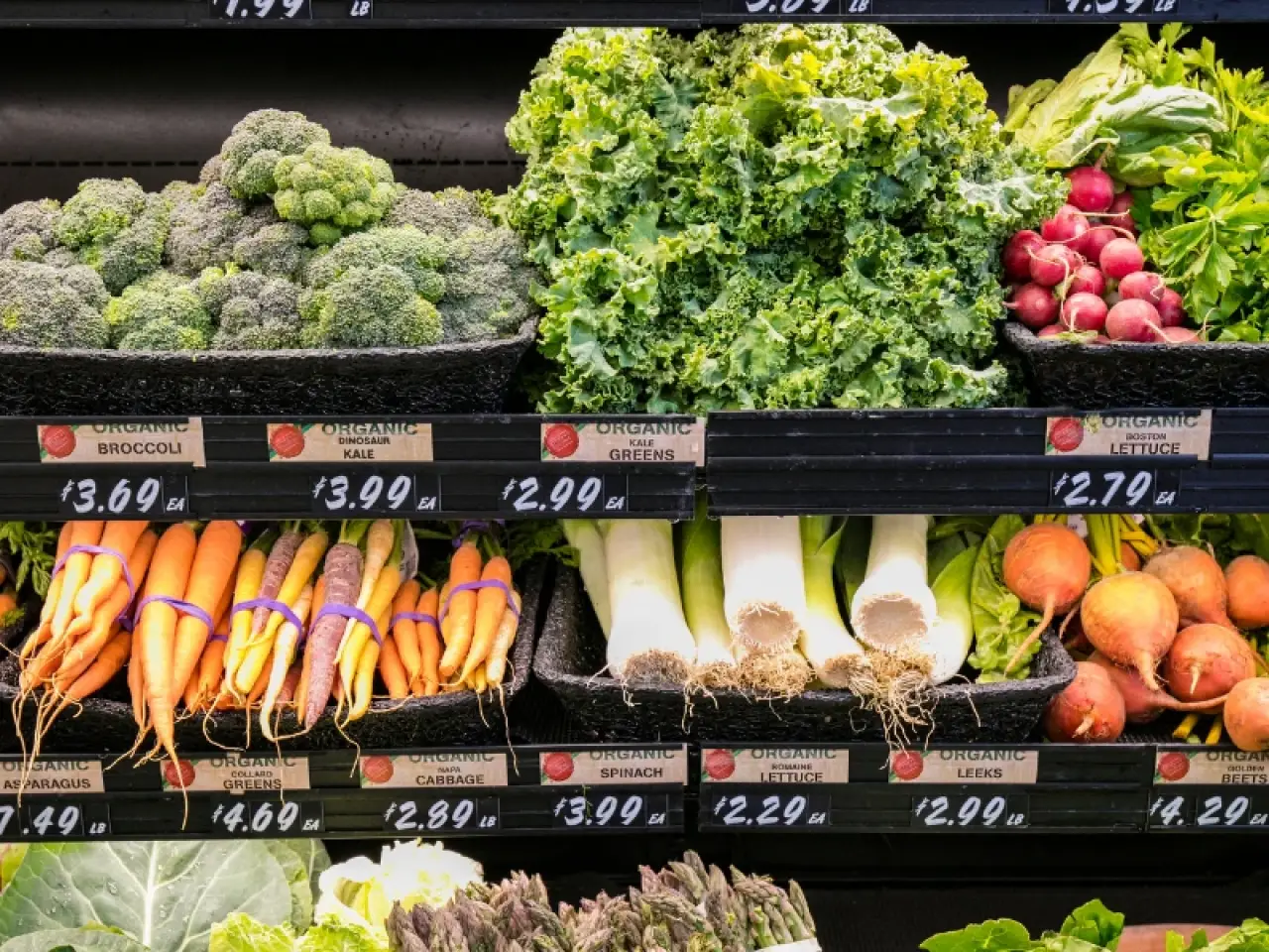 A grocery display with broccoli, kale, lettuce, carrots, leeks, radishes, and other produce.