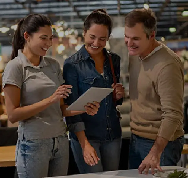 three neutrally dressed adults hover around a tablet at a specialty store