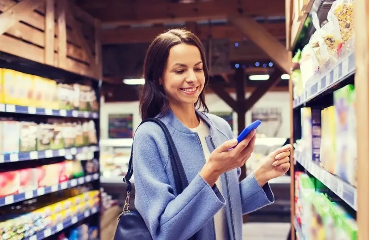 woman in blue coat holding phone in grocery store aisle