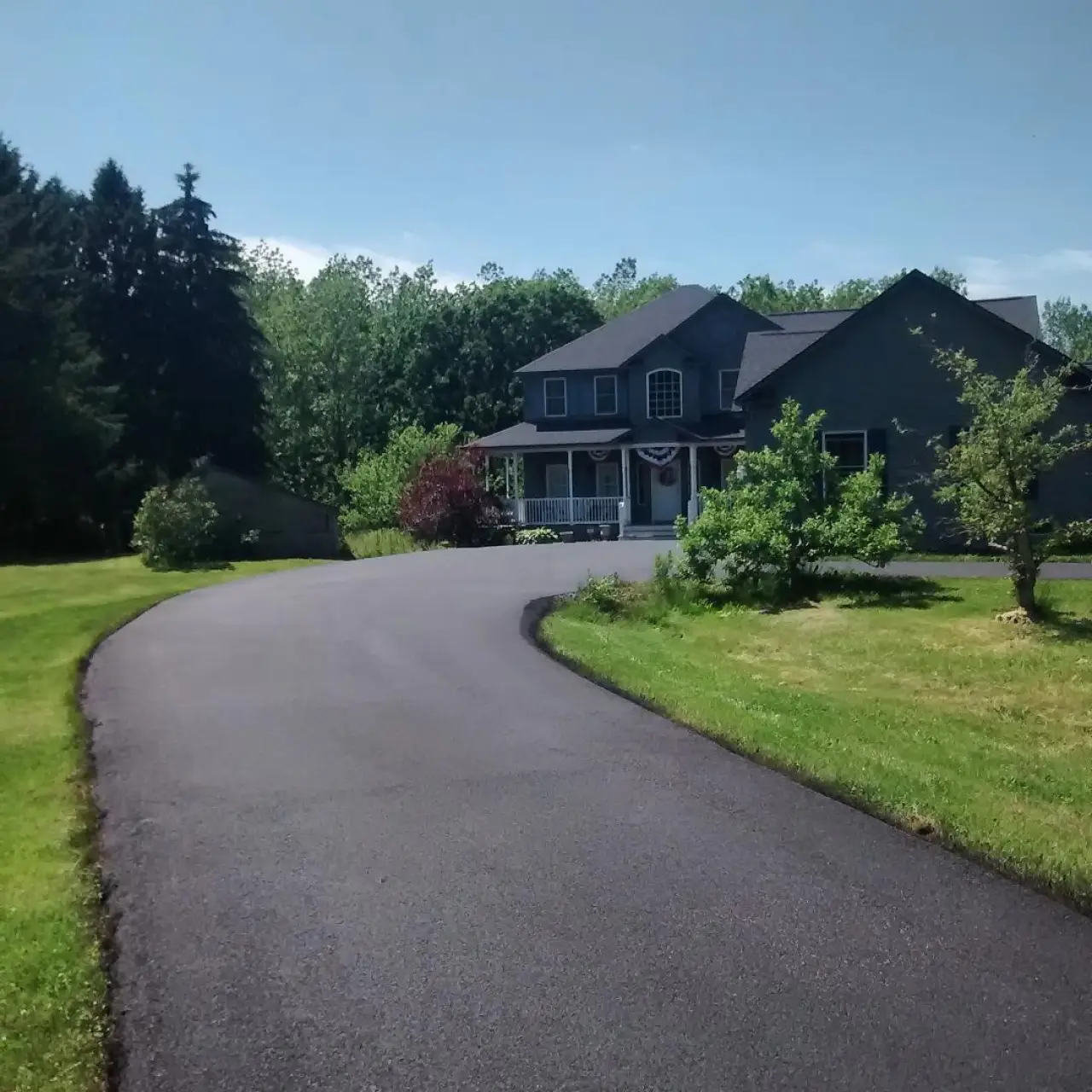 A newly-paved driveway in front of a blue farmhouse.