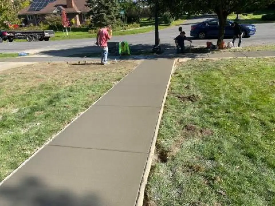 Freshly poured concrete sidewalk with people working and sitting nearby on a sunny day.
