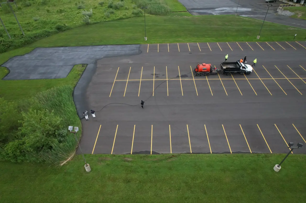 A crew seals cracks in an empty parking lot with equipment and a truck on site.