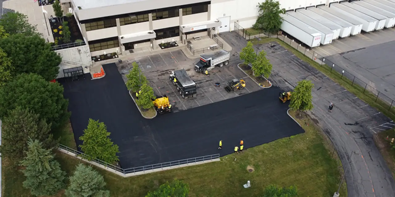 An aerial view of a new asphalt parking lot with workers and work trucks.
