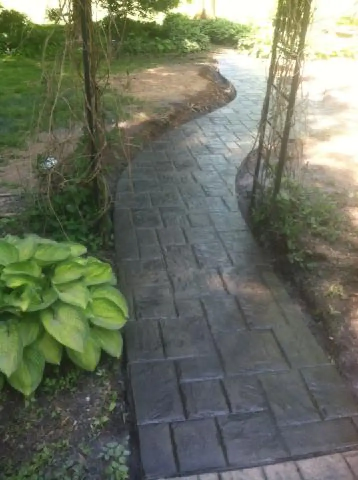 Curved stone garden path bordered by greenery and an archway, leading into sunlight.