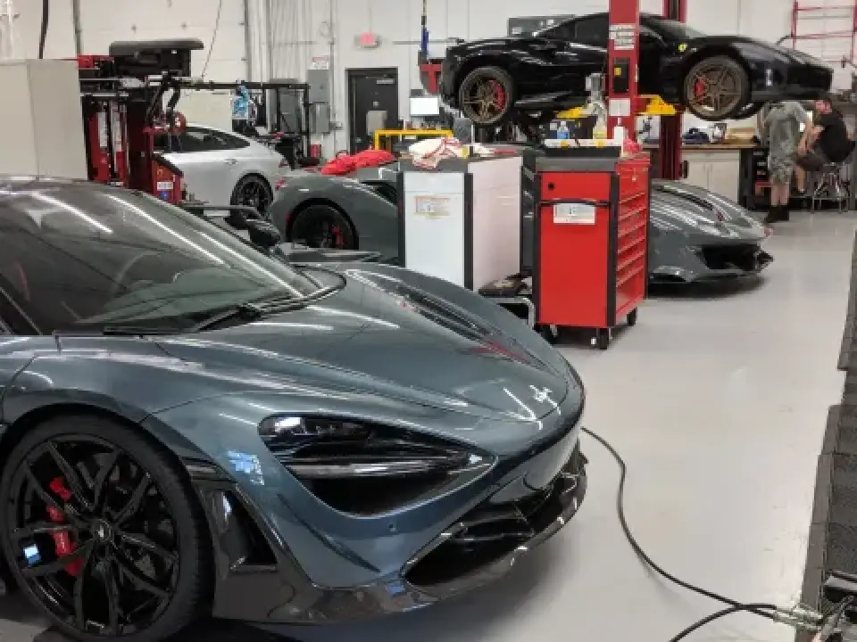 Multiple luxury sports cars in an auto repair shop, with tools and lifts visible in the background.