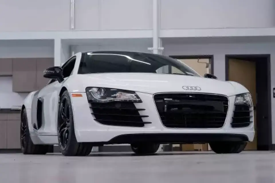 A white Audi R8 sports car parked indoors in a modern, clean garage or showroom.