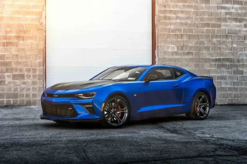 A blue sports car parked in front of a large garage door and a brick wall.