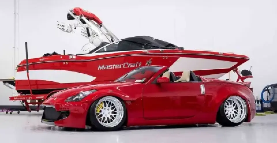 A red sports car and a red MasterCraft speedboat parked side by side in a white garage.