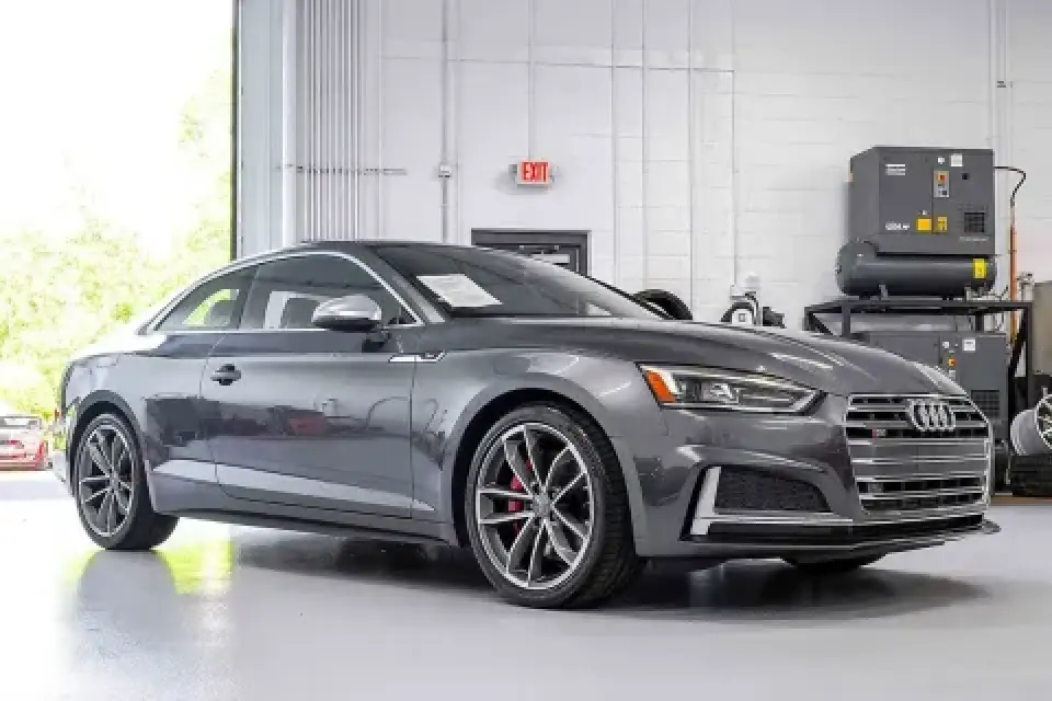 A gray Audi coupe parked indoors in a clean, well-lit garage or automotive shop.