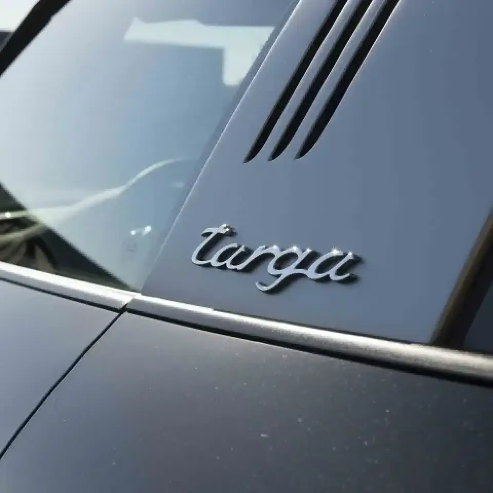 Close-up of a car with the targa badge on a glossy black pillar near the rear window.