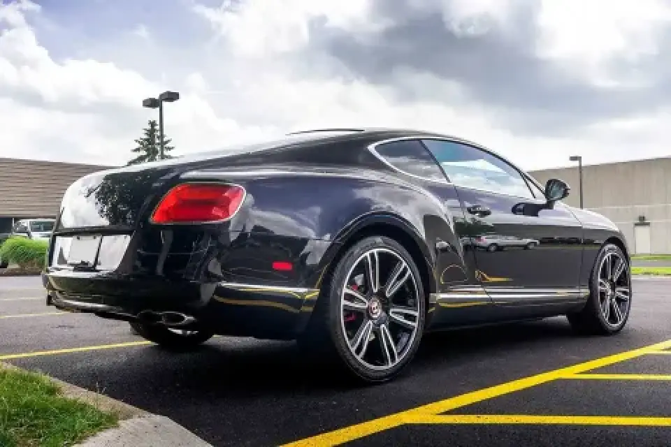 A black luxury coupe parked in a lot with yellow lines, shown from the rear side angle.