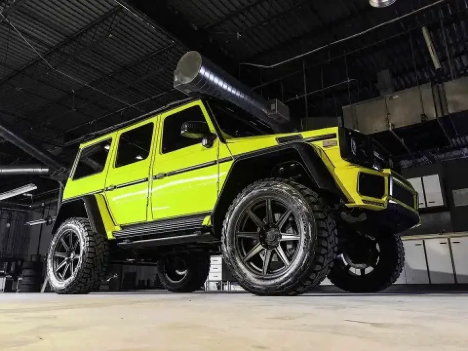Neon yellow Mercedes-Benz G-Class SUV with large off-road tires parked indoors under lights.