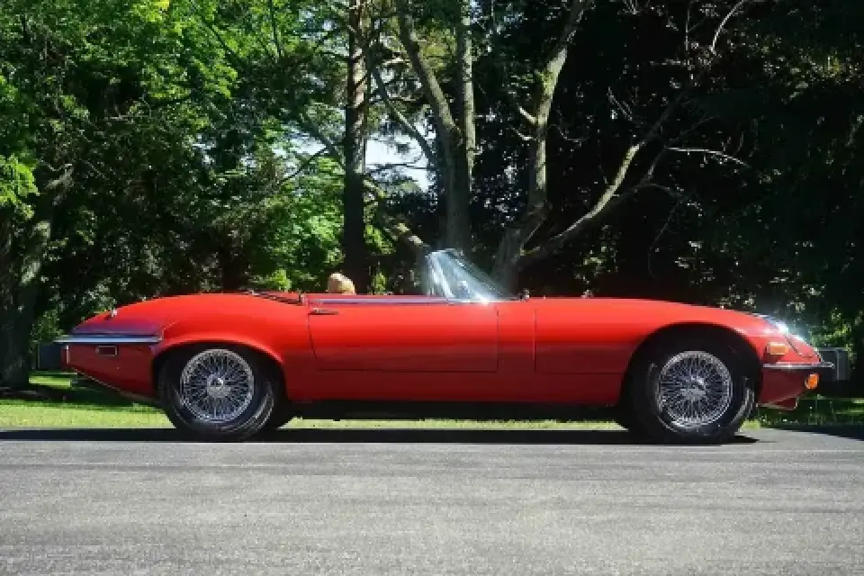 A classic red convertible car parked on a road with trees and grass in the background.
