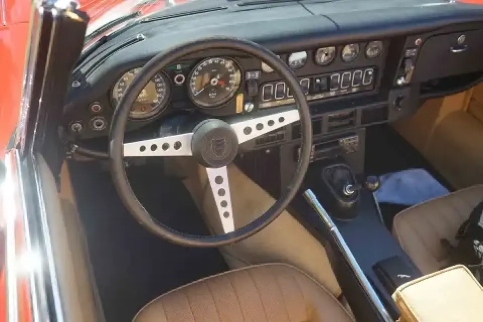 Classic car interior with a vintage steering wheel, gauges, and tan leather seats.