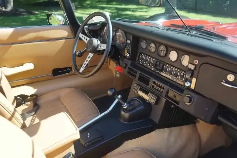 Tan leather interior and dashboard of a classic car with manual gear shift and round gauges.