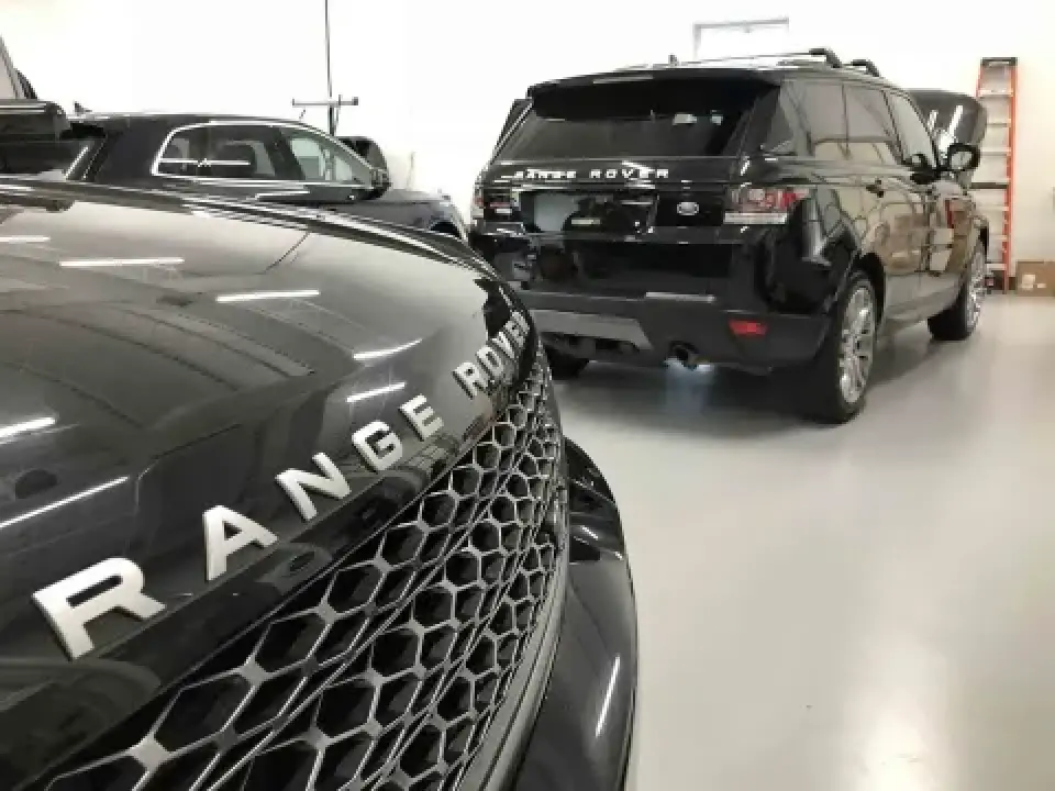 Two black Range Rovers parked indoors on a clean, white floor, facing opposite directions.