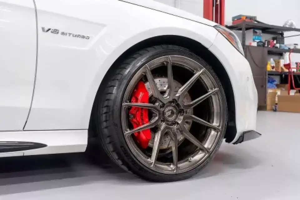 Close-up of a car’s front wheel with a red brake caliper and V8 BITURBO badge on fender.