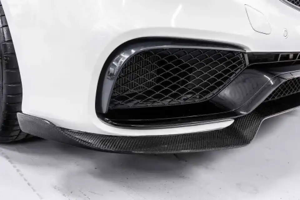 Close-up of a white cars front bumper with a black mesh grille and carbon fiber splitter.