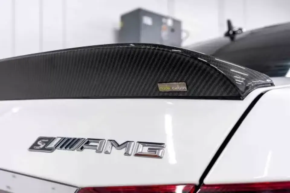Close-up of a carbon fiber spoiler and AMG badge on the rear of a white Mercedes car.
