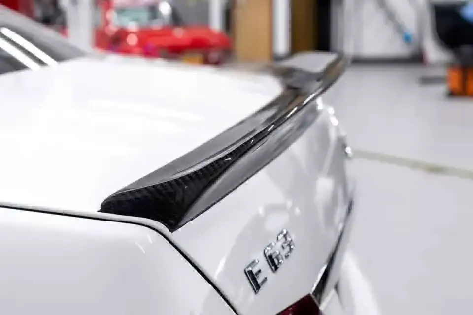 Close-up of a black carbon fiber spoiler on a white Mercedes E63 sedan in a garage.