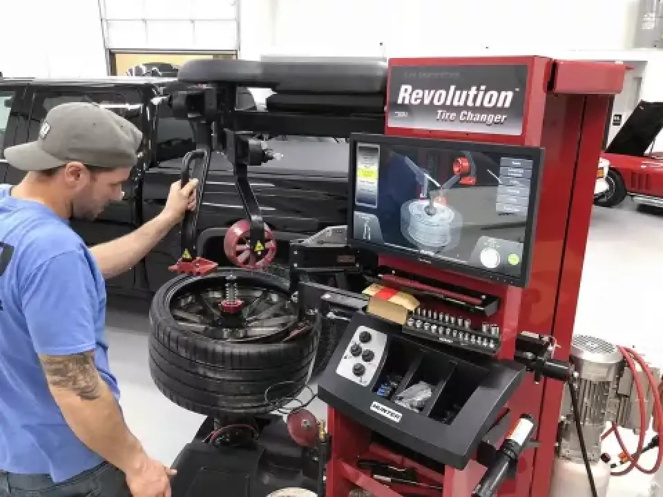 A man operates a Revolution tire changer machine to change a tire in an auto shop.