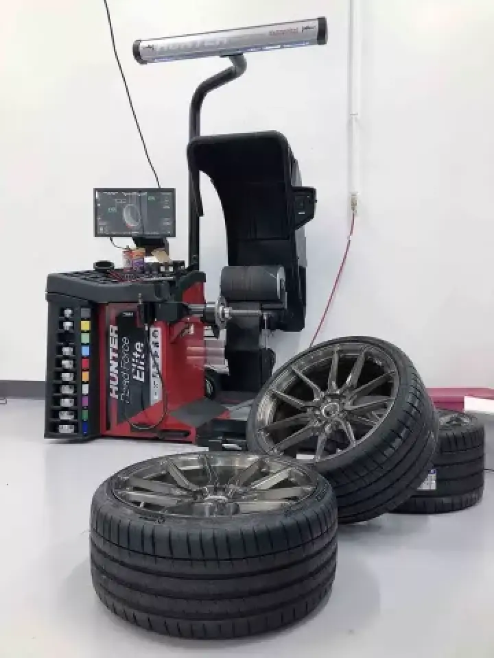 A tire balancing machine stands behind three car tires stacked on a clean shop floor.