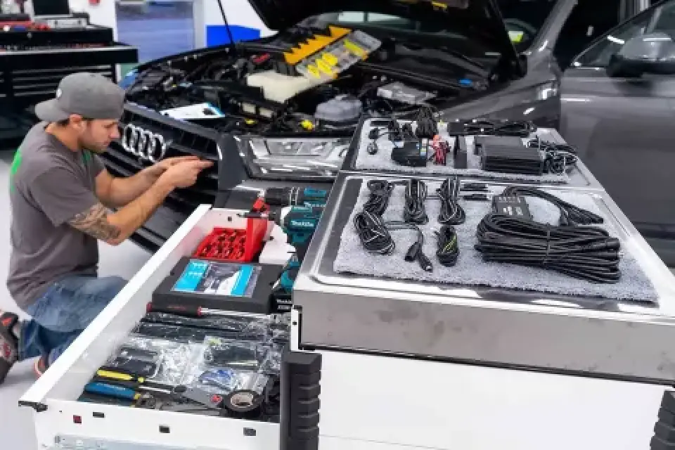 Man working on Audi car with hood open; tool drawer and cables visible in foreground.