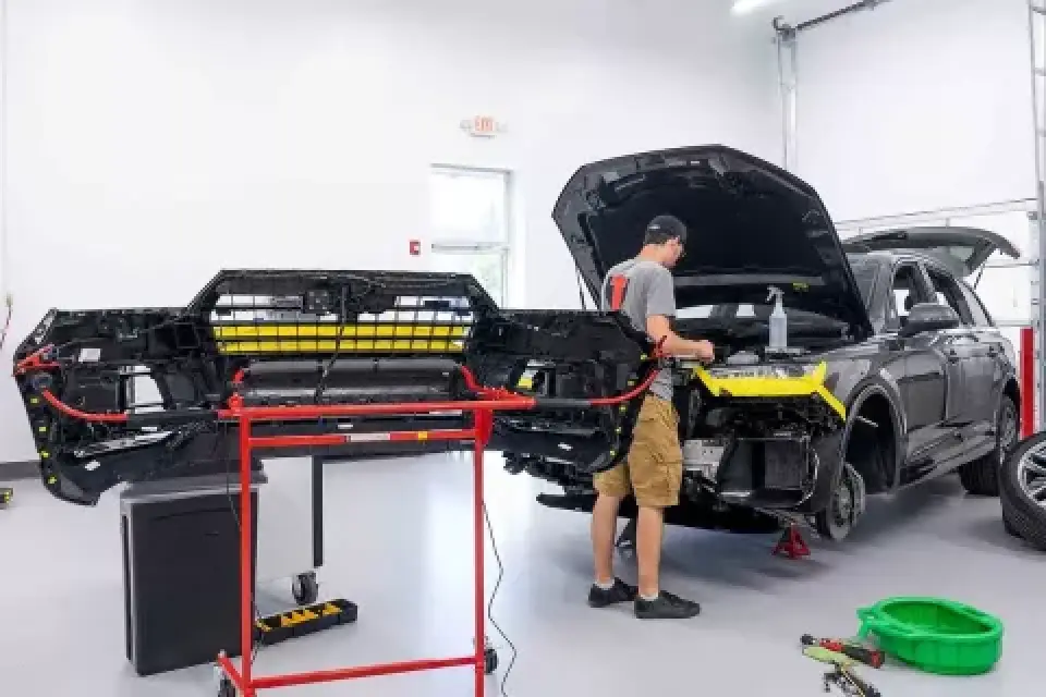 A man repairs an SUV with its front bumper removed in an auto workshop.