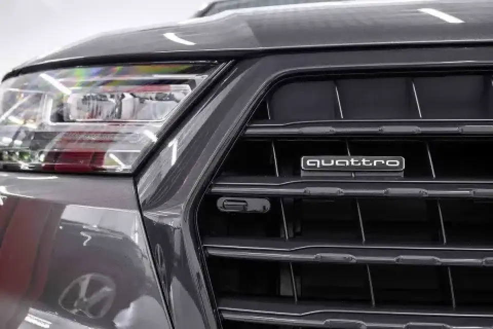 Close-up of a cars front grille and headlight with a quattro badge on the grille.