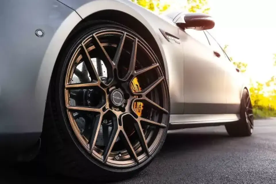 Close-up of a cars bronze alloy wheel and tire, parked on a sunlit paved surface.