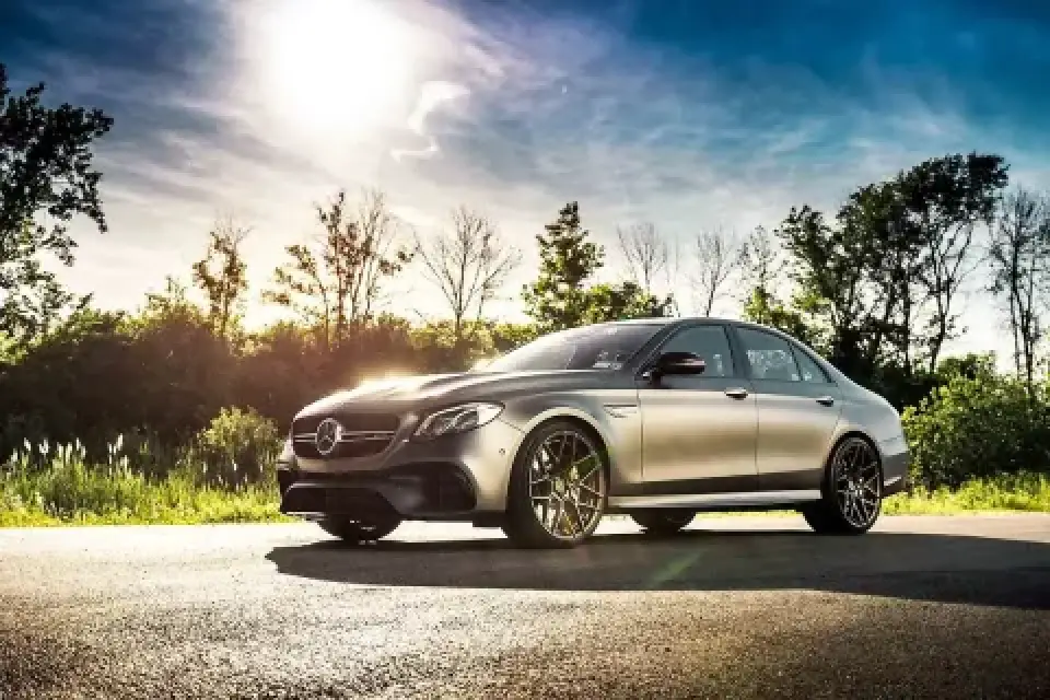 A silver Mercedes-Benz sedan parked on a sunlit road with trees in the background.