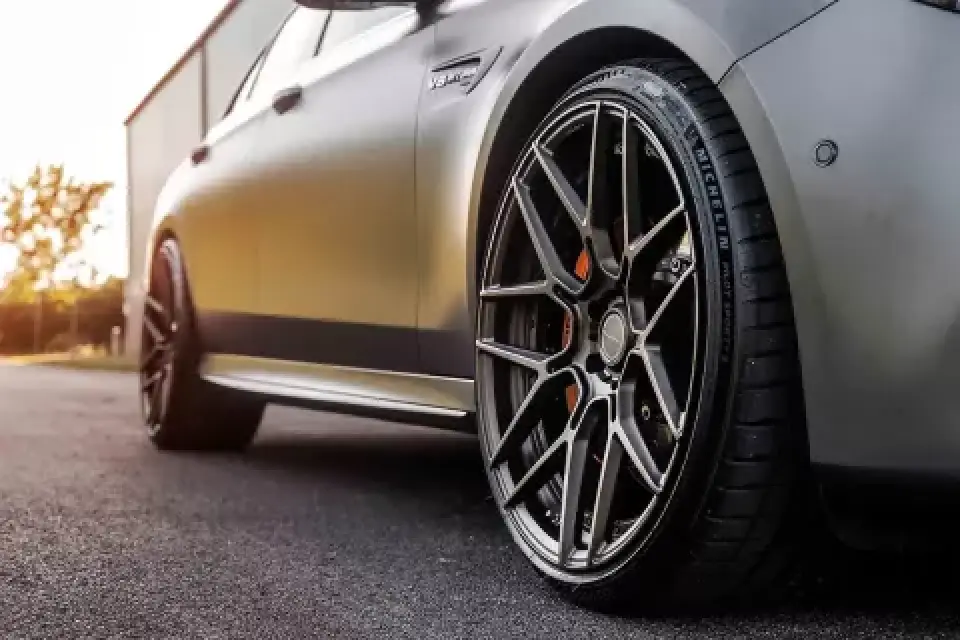 Close-up of a luxury car wheel with black alloy rims parked on an asphalt surface.