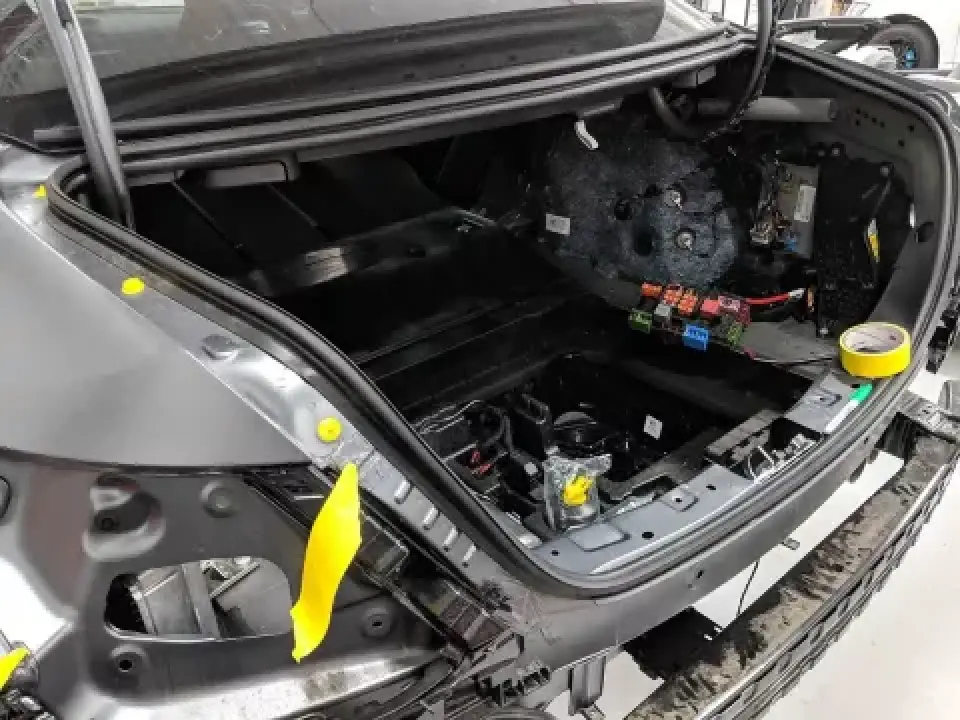 Car trunk with interior panels removed, exposing wiring, fuses, and electrical components.