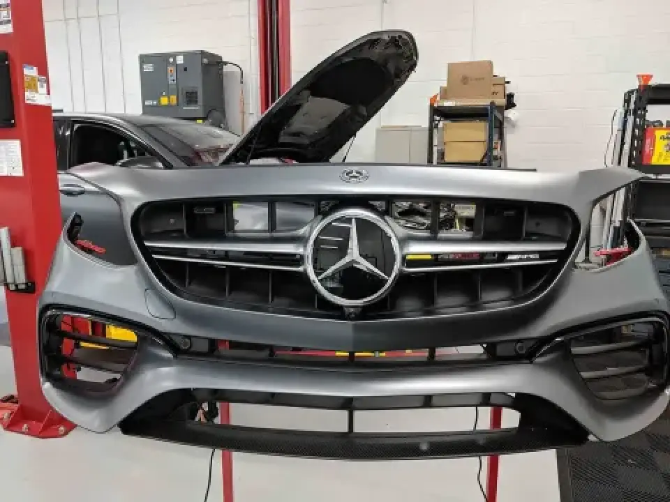 A gray Mercedes-Benz with its front grille and hood open in an auto repair shop.