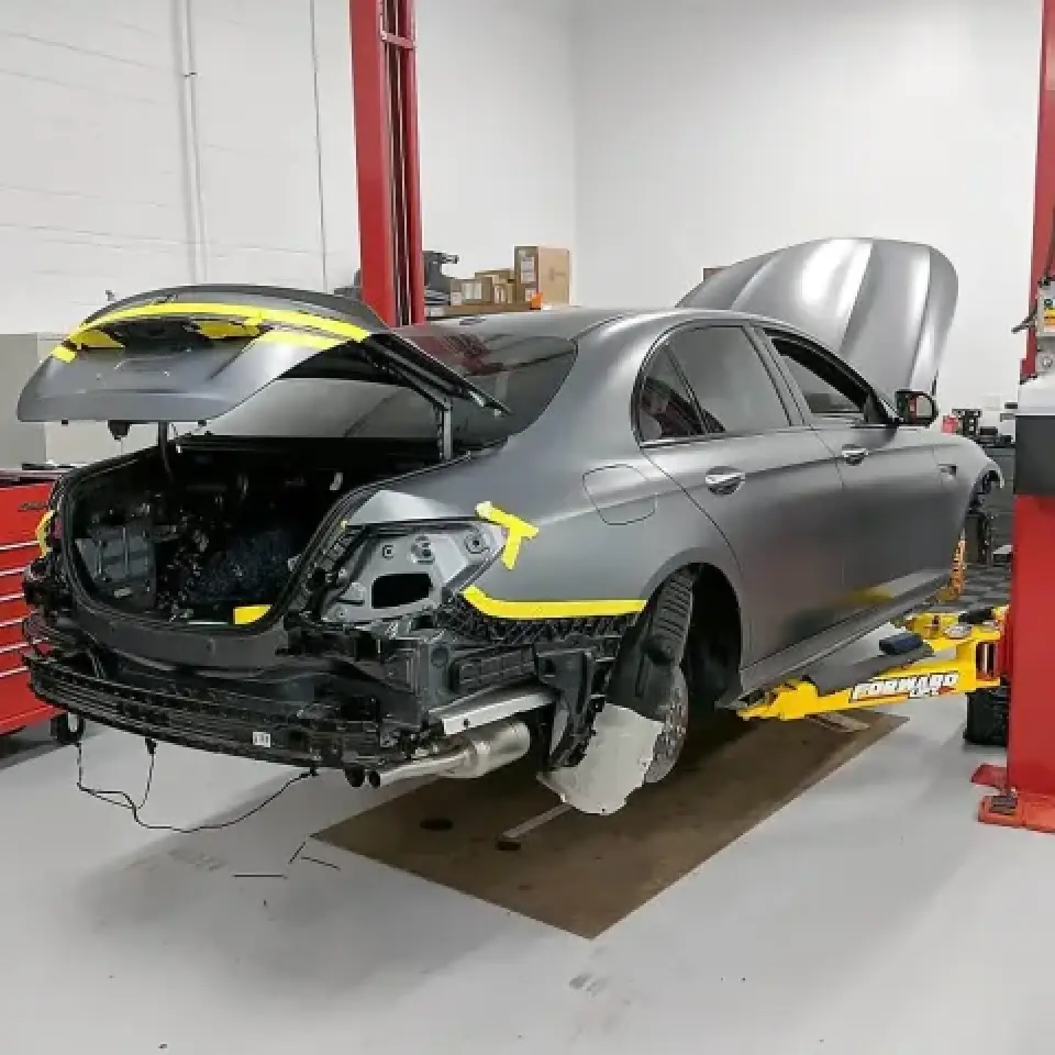 A gray car with missing rear parts is lifted on a car lift in an auto repair shop.