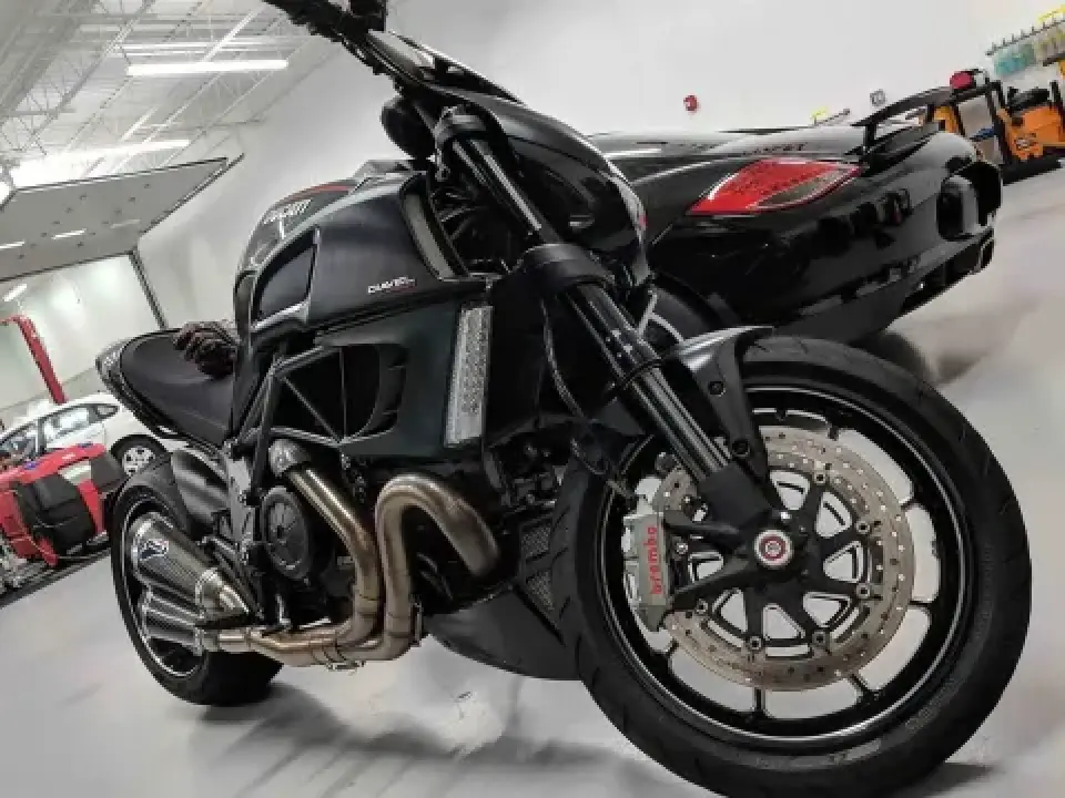 Black Ducati Diavel motorcycle parked indoors next to a black sports car in a garage.