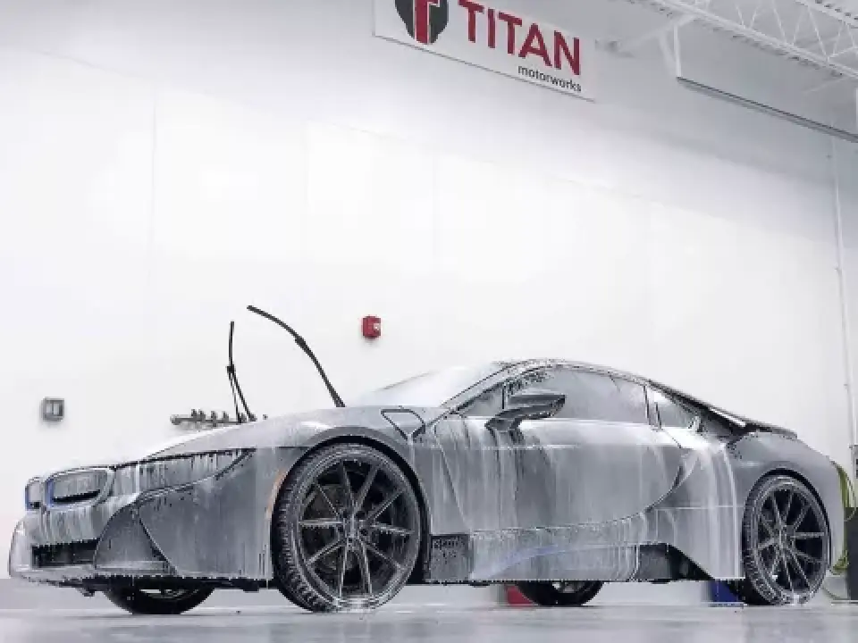 A sleek sports car covered in soap suds is being washed inside a well-lit garage.