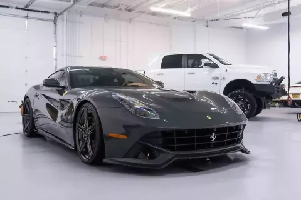 A black Ferrari and a white pickup truck parked inside a clean, well-lit garage.