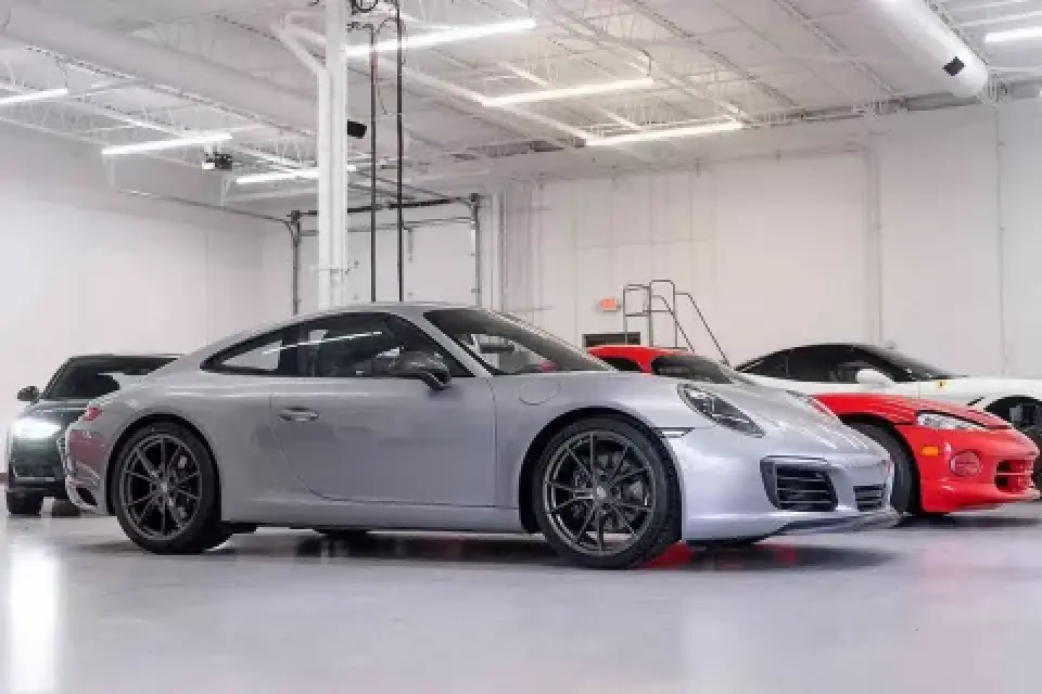 A silver sports car parked in a bright, clean garage with other cars in the background.