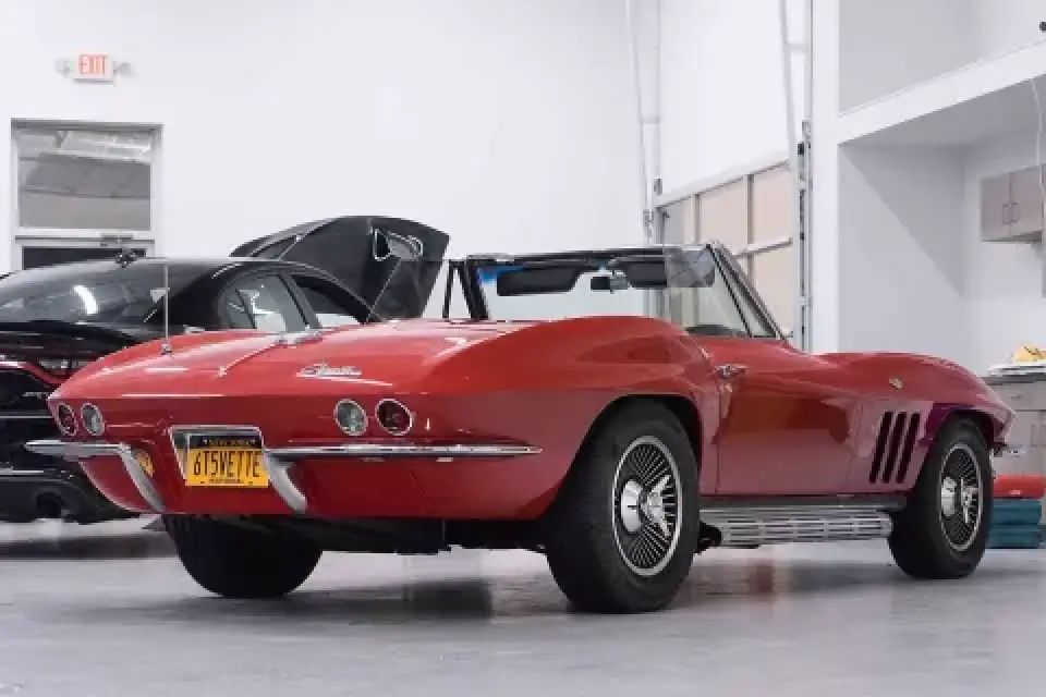 A classic red convertible car parked indoors, viewed from the rear left side.