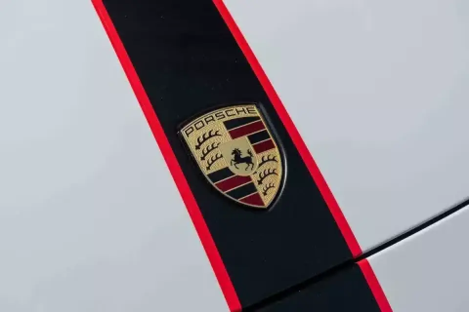 Porsche emblem on a white car hood with a black and red racing stripe.