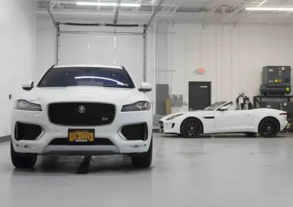 Two white Jaguar cars parked in a clean, brightly lit garage with gray floors and white walls.