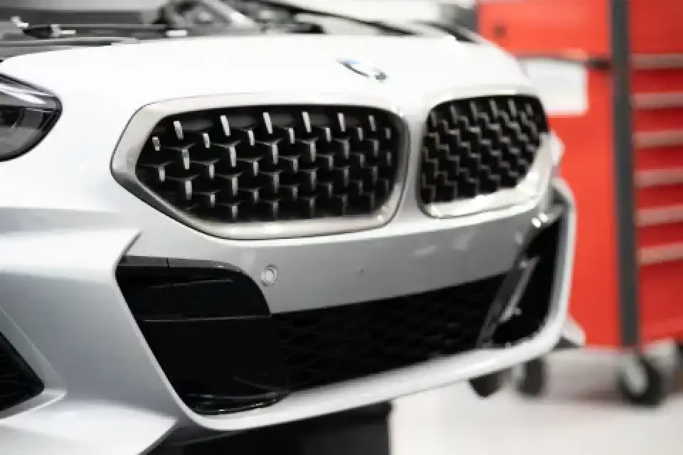 Close-up of the front grille and bumper of a silver BMW car with a red tool chest in background.