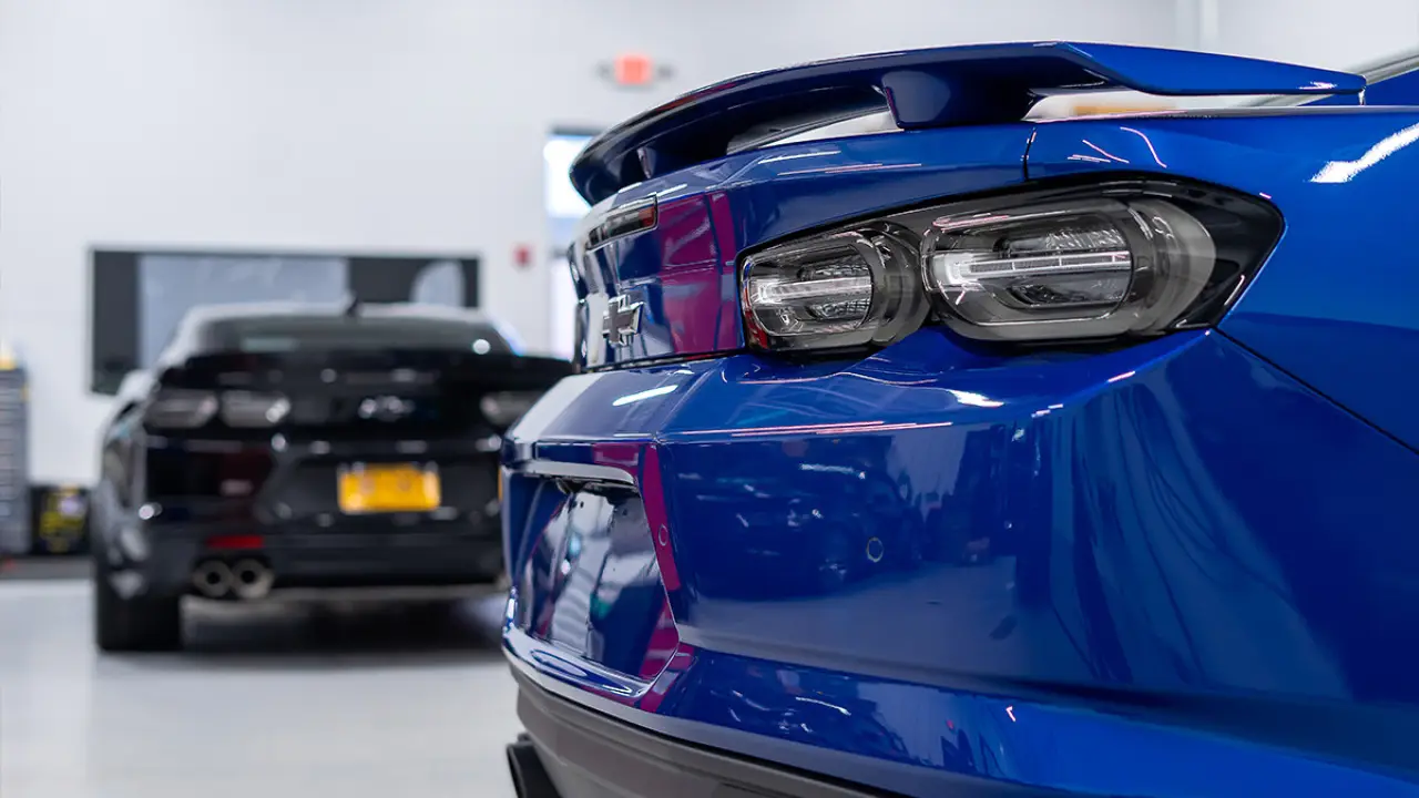 Close-up of a blue sports car’s taillight, with a black car blurred in the background.