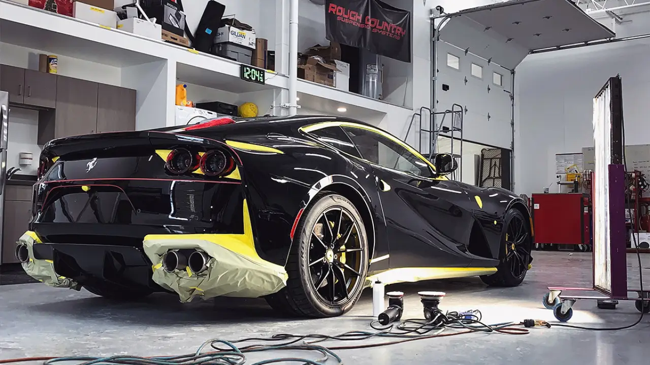 A black Ferrari sports car is being detailed in a garage with masking tape on its edges.