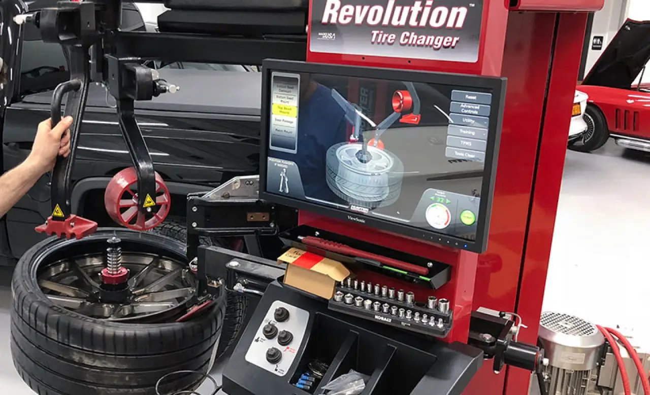 A technician uses a Revolution tire changing machine next to a car in an auto repair shop.