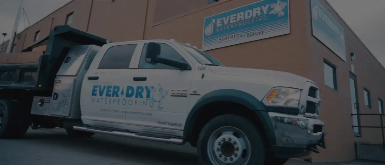 A white Everdry Waterproofing truck parked in front of a building with the company’s sign.