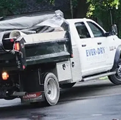 A white Everdry truck with a covered load is parked on a residential street.