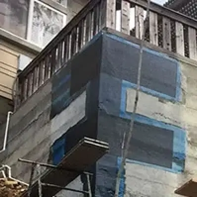 A partially covered exterior wall with black and blue weatherproofing material and scaffolding.