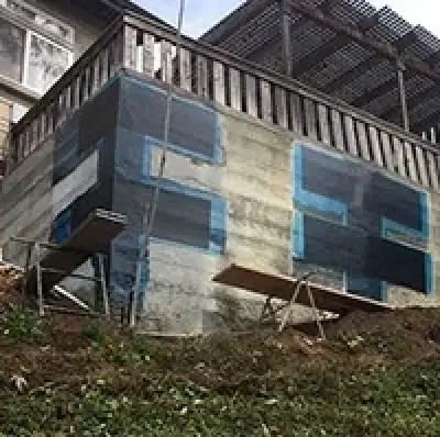 A retaining wall on a slope, partially covered with black waterproofing membrane and scaffolding.